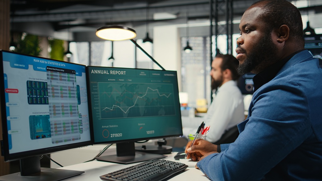 An African American financial analyst writing growth strategy notes on a textbook, working in business office with insights and financial data.